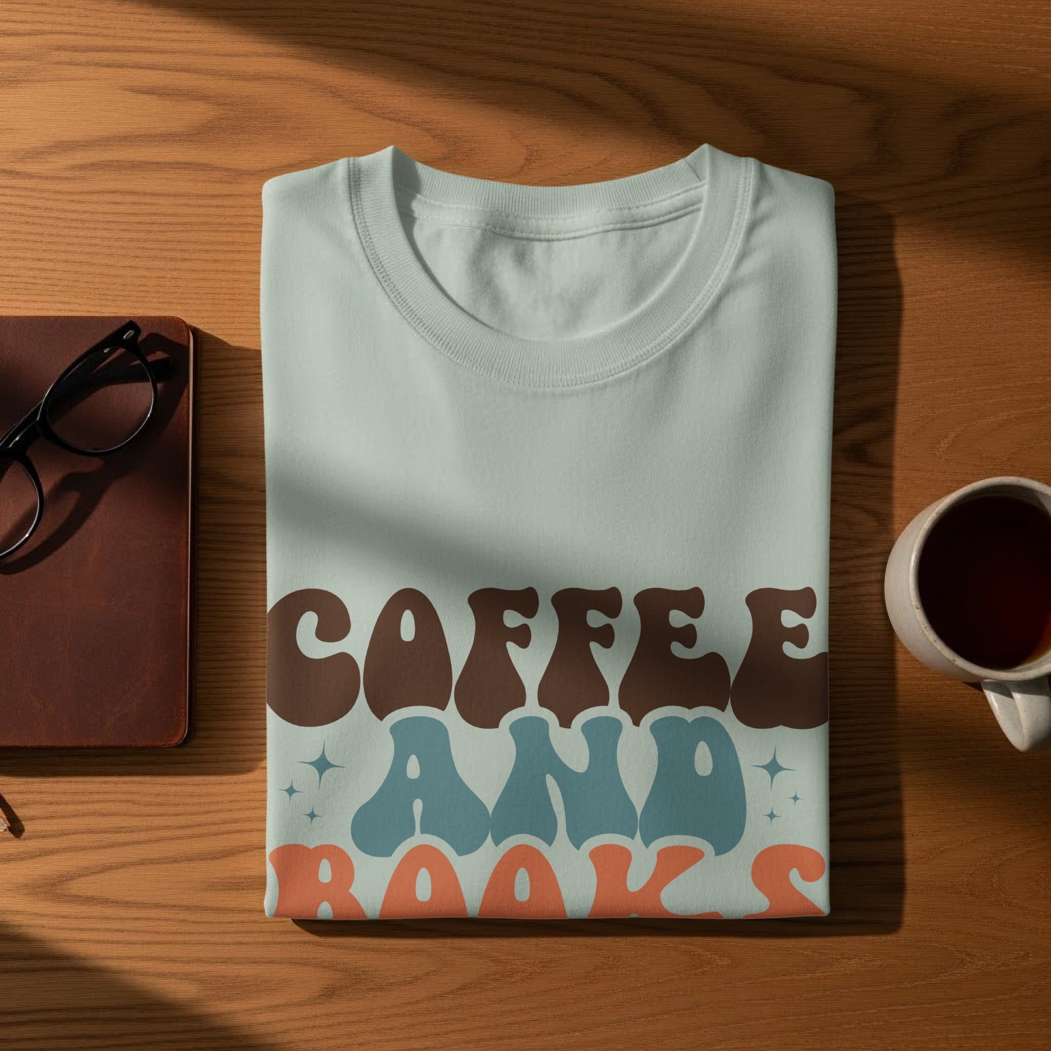 Light blue t-shirt with "COFFEE AND BOOKS" text in brown, blue, and orange retro font.