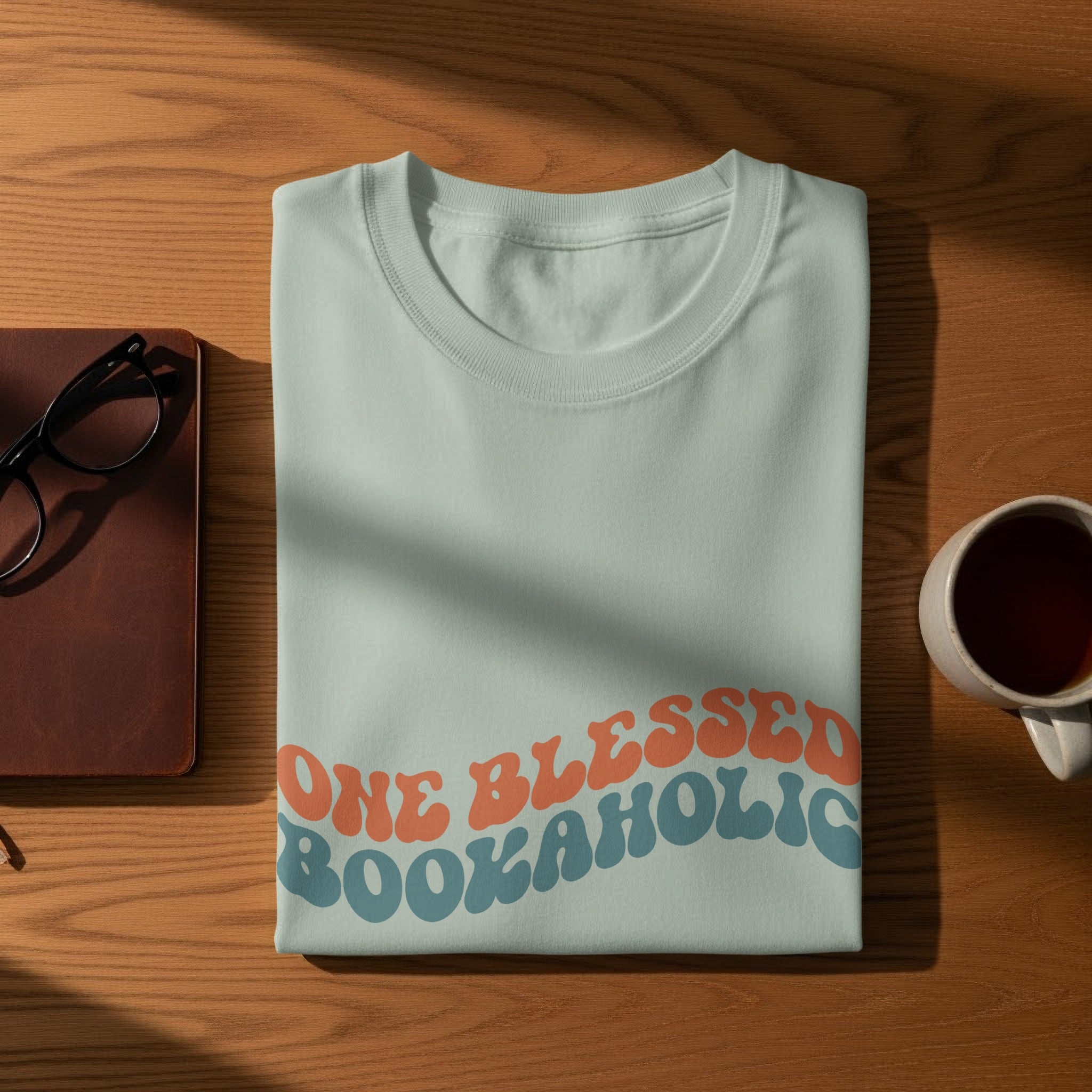 Light blue t-shirt with "ONE BLESSED BOOKAHOLIC" in wavy orange and blue text.