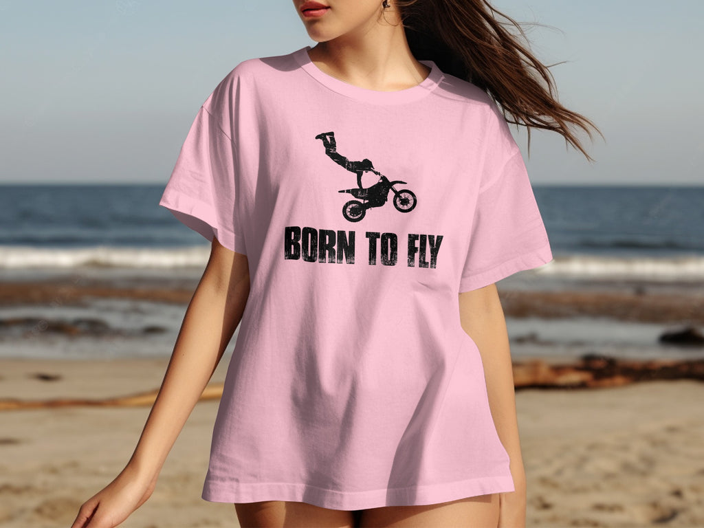 Pink t-shirt with black motocross rider and text "BORN TO FLY" on beach background.