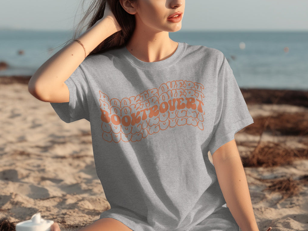 Grey t-shirt with orange text that reads "Book Lover" on a beach.