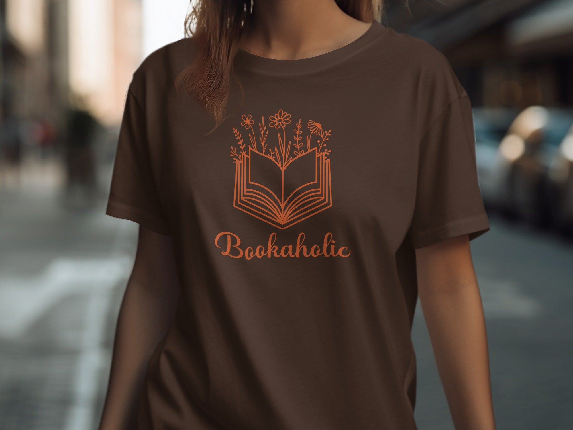 Brown t-shirt with an orange outline of an open book and flowers, reading "Bookaholic".