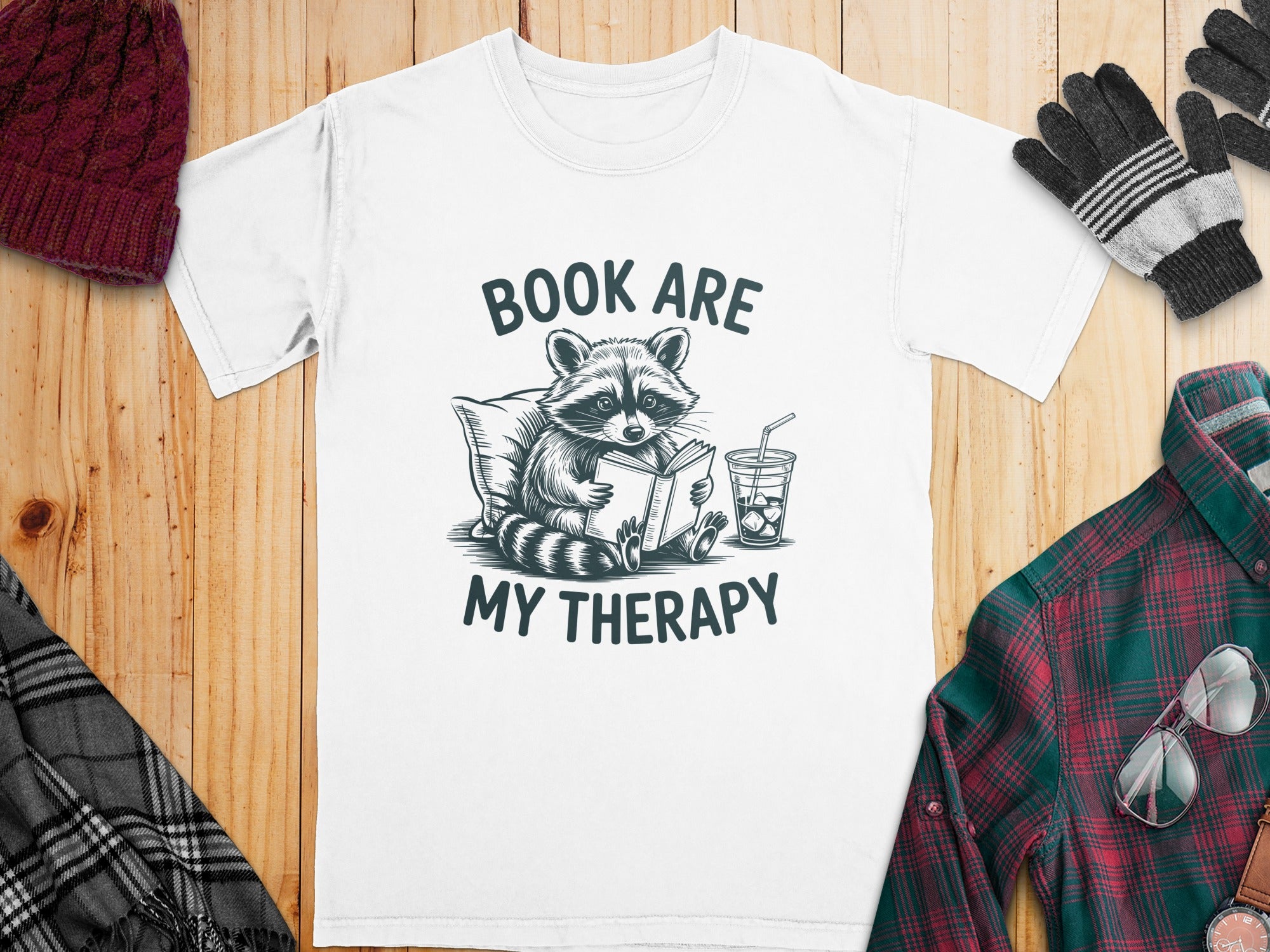 White t-shirt with a raccoon reading a book, text "BOOK ARE MY THERAPY".