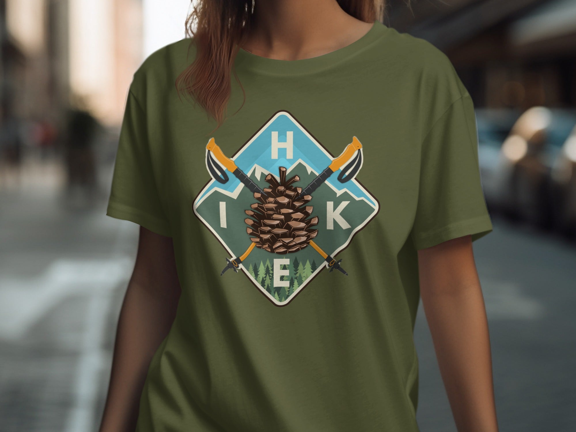 Olive green t-shirt with "HIKE" text, pine cone, crossed poles, and mountains graphic.