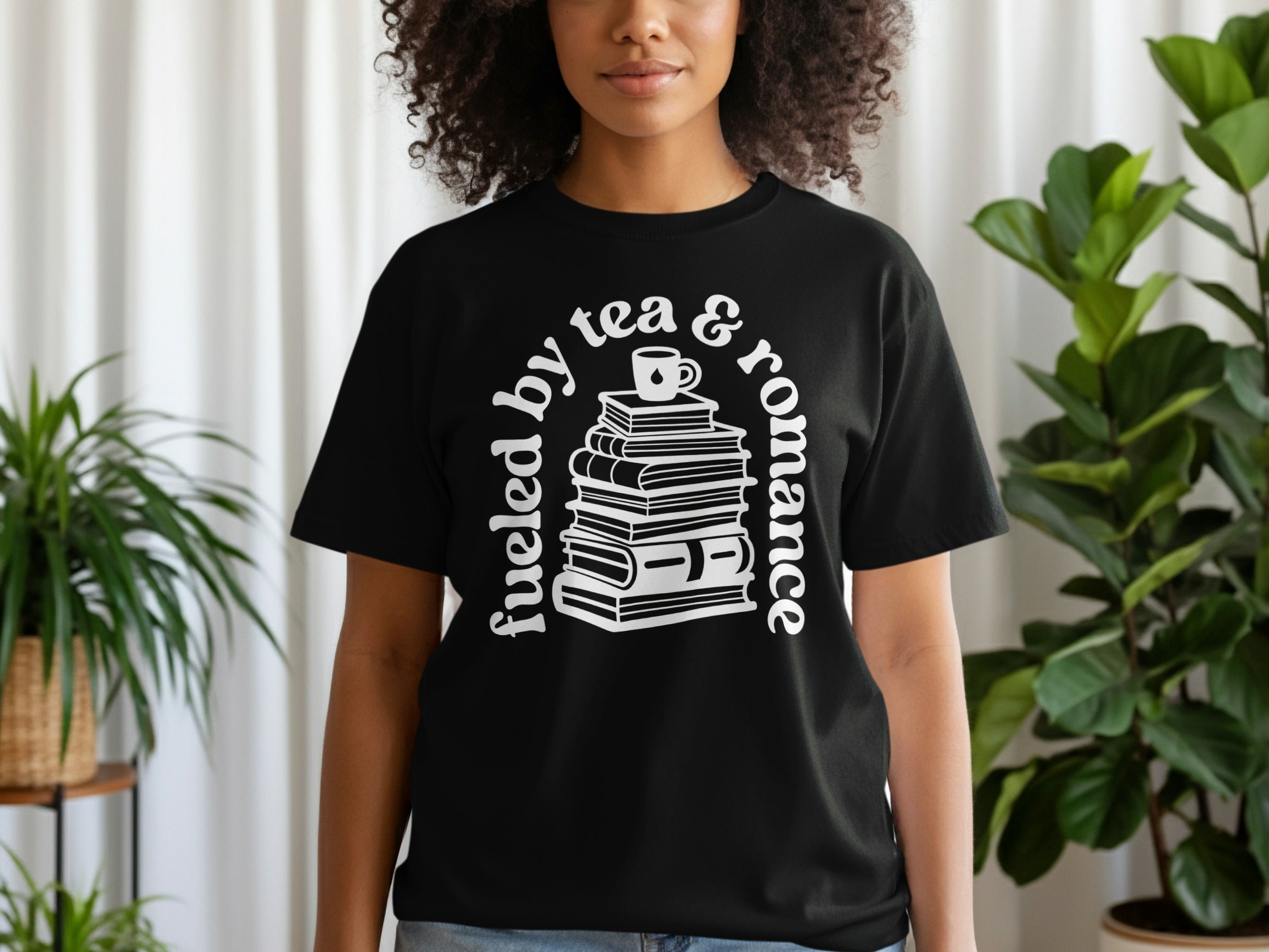 Black t-shirt with white text "fueled by tea & romance" and stack of books.
