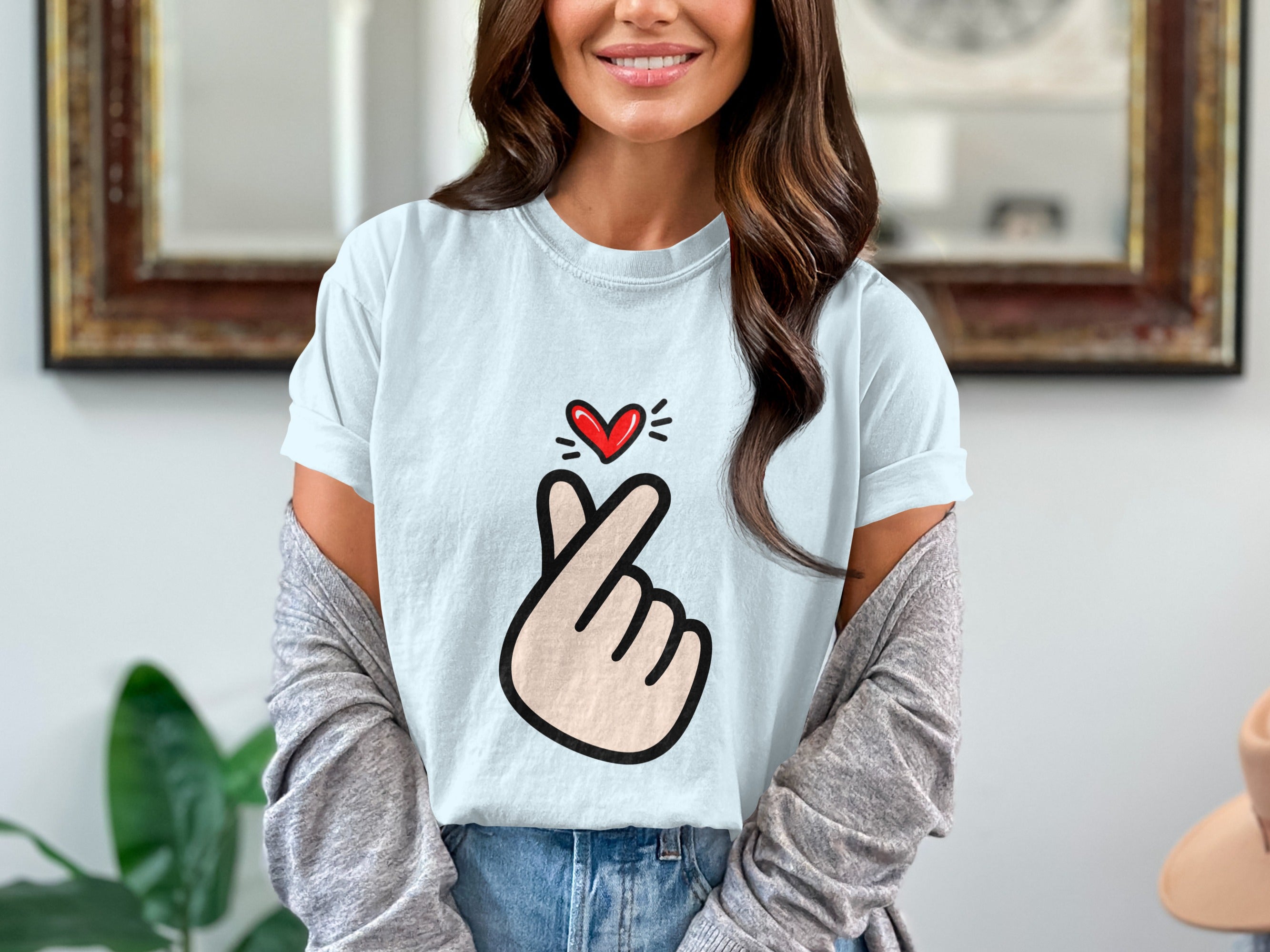 Light blue t-shirt with a red heart and finger heart cartoon graphic.