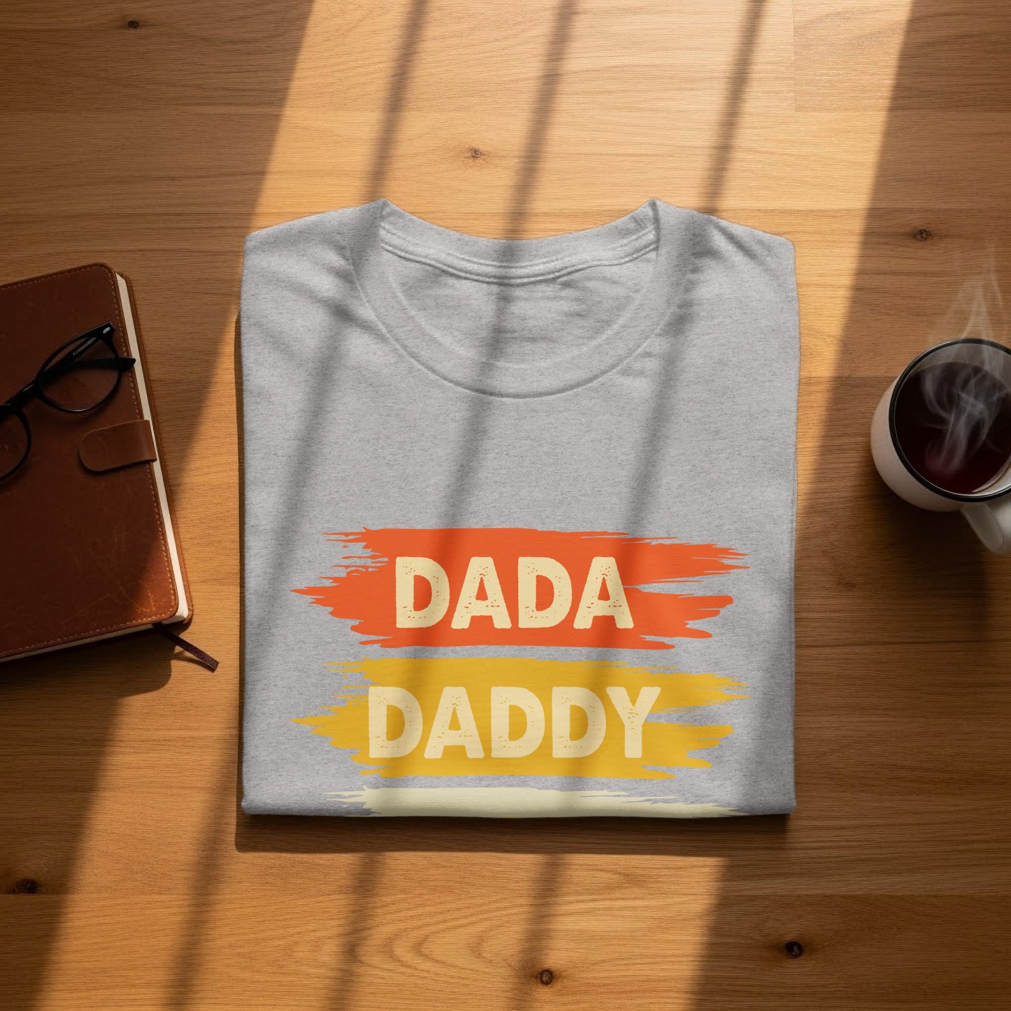 Grey t-shirt with painted "DADA" and "DADDY" text on wooden surface.