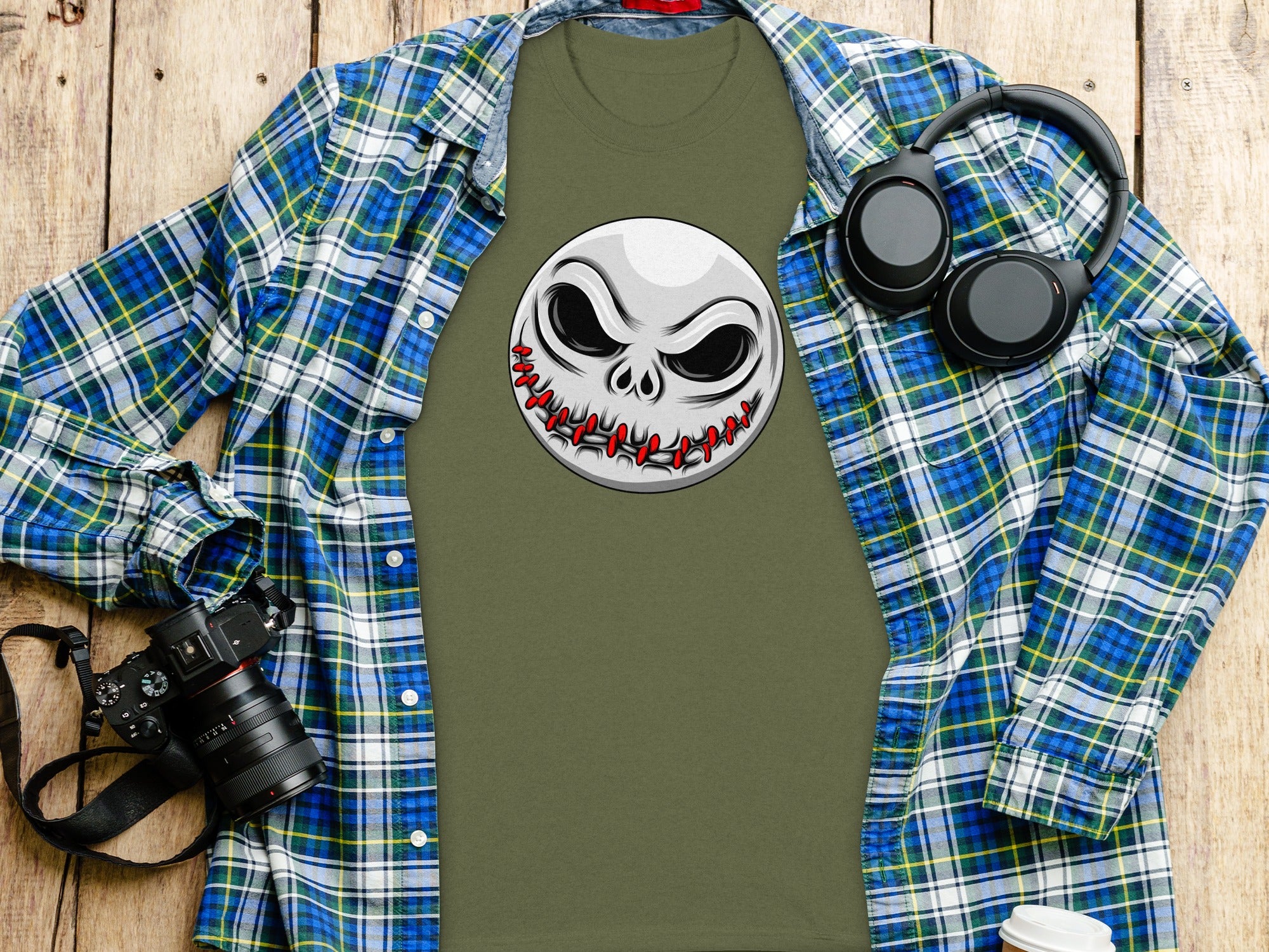 Olive t-shirt with stitched mouth Jack Skellington graphic, plaid shirt, headphones, camera.