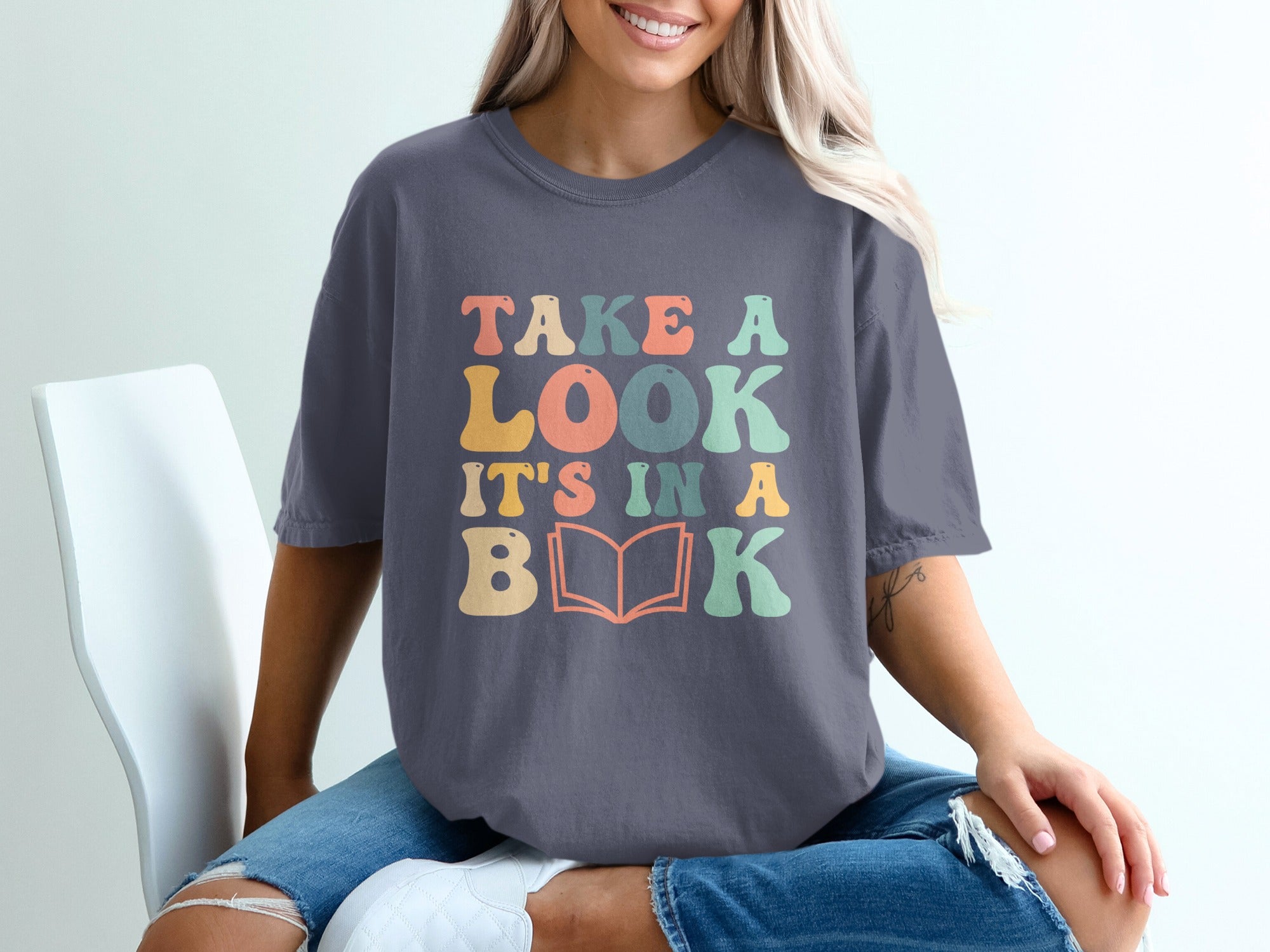 Dark grey t-shirt with colorful text that reads "TAKE A LOOK IT'S IN A BOOK."