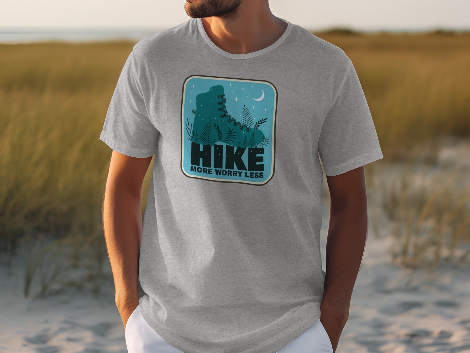 Grey t-shirt with a blue graphic featuring a hiking boot, ferns, moon, and text "HIKE MORE WORRY LESS".