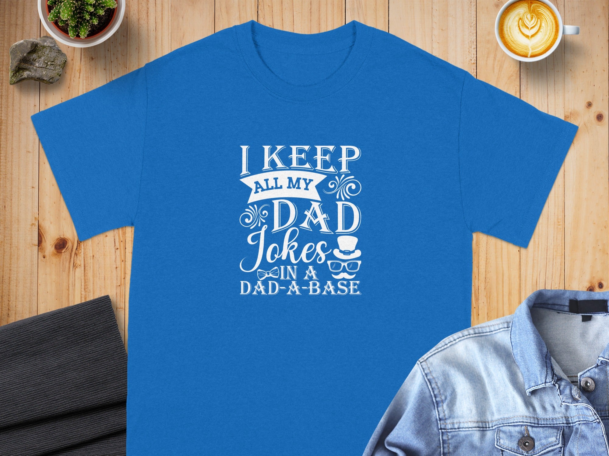 Blue t-shirt with white text reading "I KEEP ALL MY DAD Jokes IN A DAD-A-BASE".