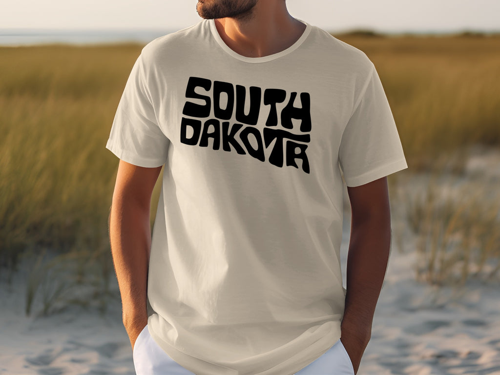 Cream t-shirt with black wavy "South Dakota" text on a beach background.