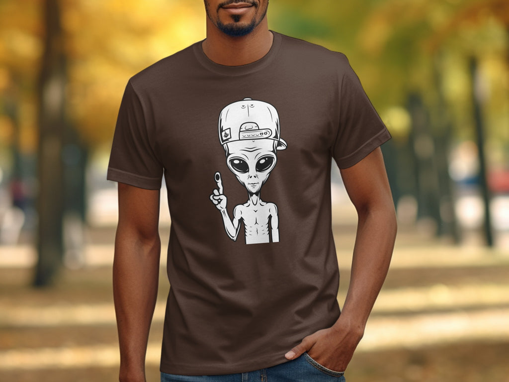 Brown t-shirt with white alien graphic wearing a backward baseball cap.