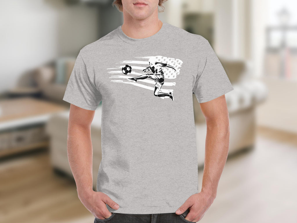 Soccer player kicking ball with abstract USA flag design on gray t-shirt.
