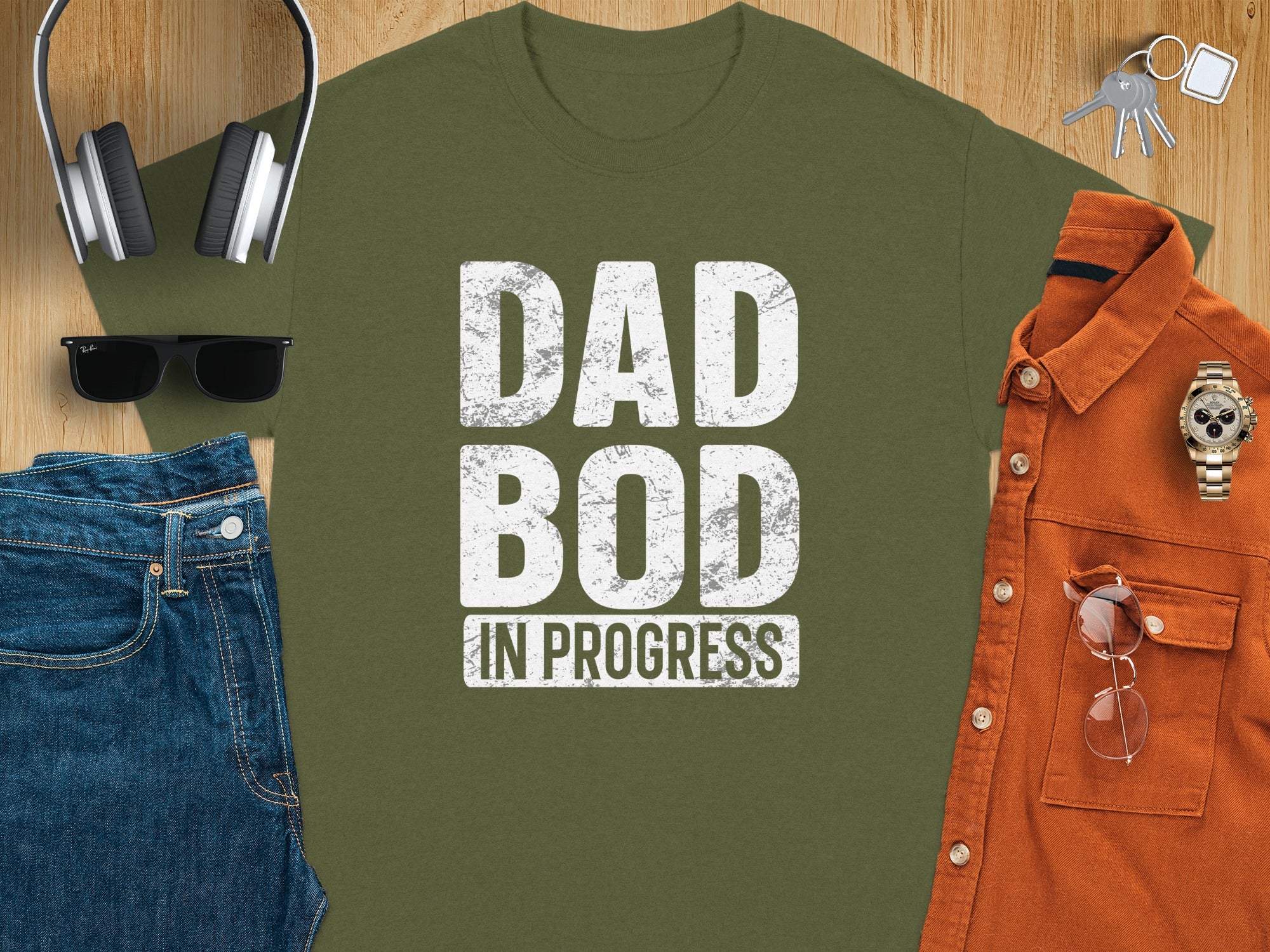 Green t-shirt with "DAD BOD IN PROGRESS" text, jeans, shirt, headphones, and accessories.