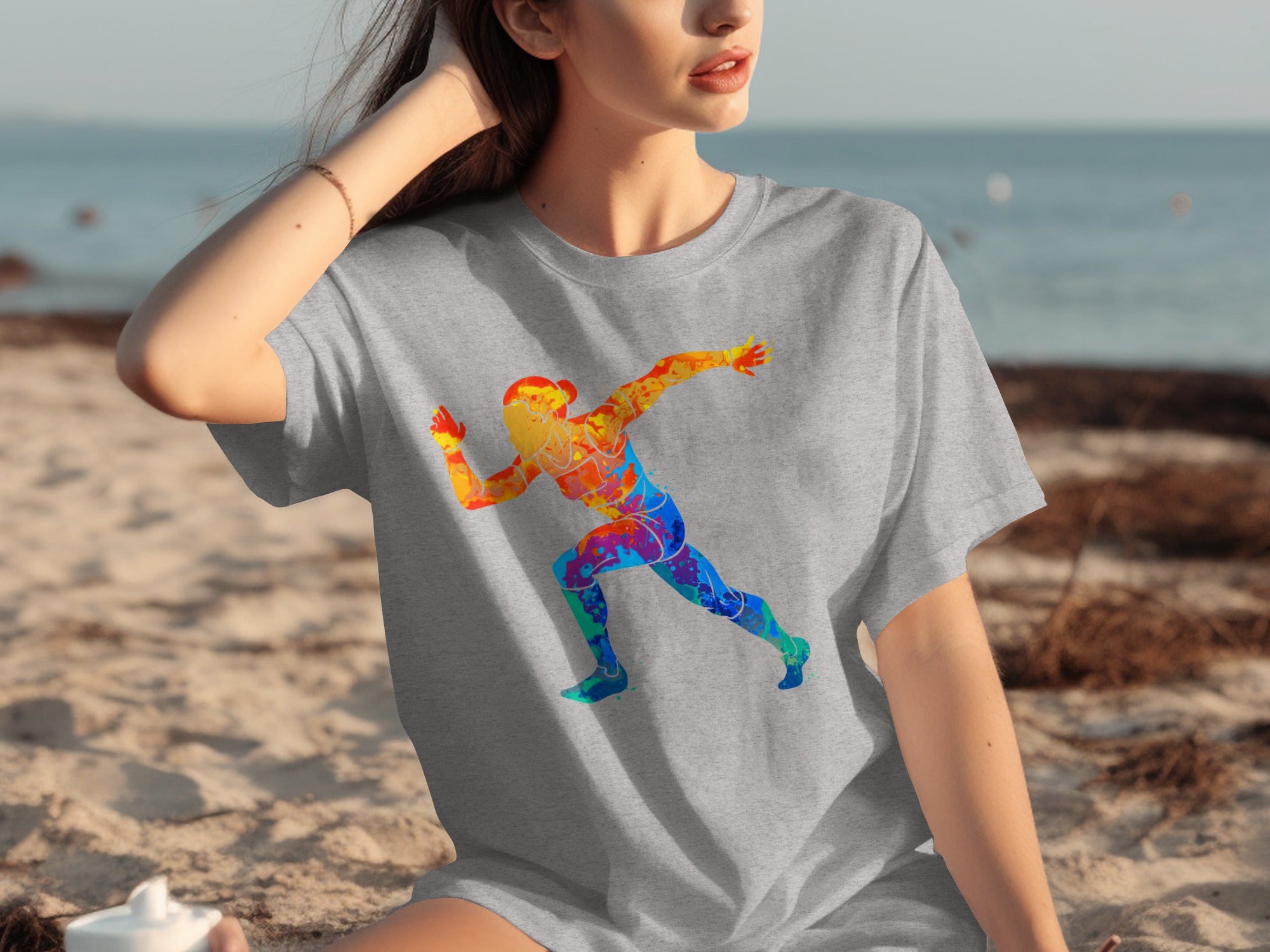 Grey t-shirt with a colorful running figure graphic on a beach.