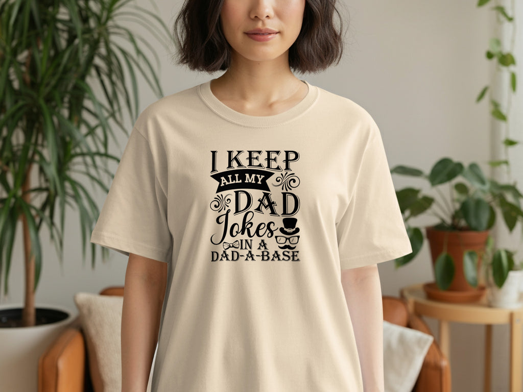Light beige t-shirt with black text "I KEEP ALL MY DAD Jokes IN A DAD-A-BASE".