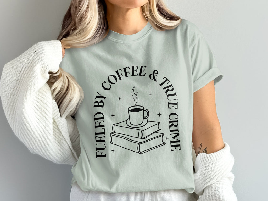 Light green t-shirt with arched text "Fueled by Coffee & True Crime" and an illustration.