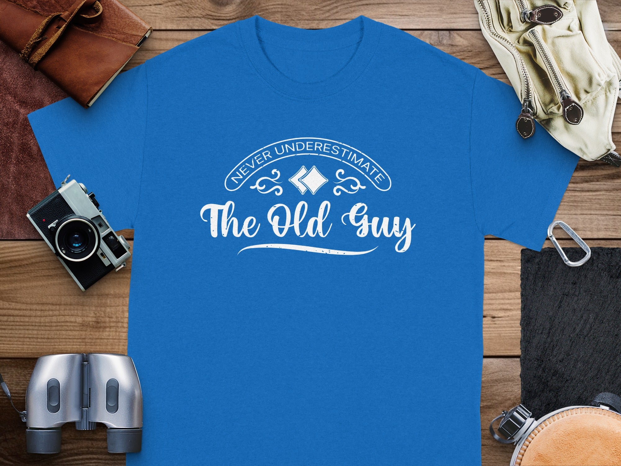 Blue t-shirt with white text "Never Underestimate The Old Guy" and decorative elements.