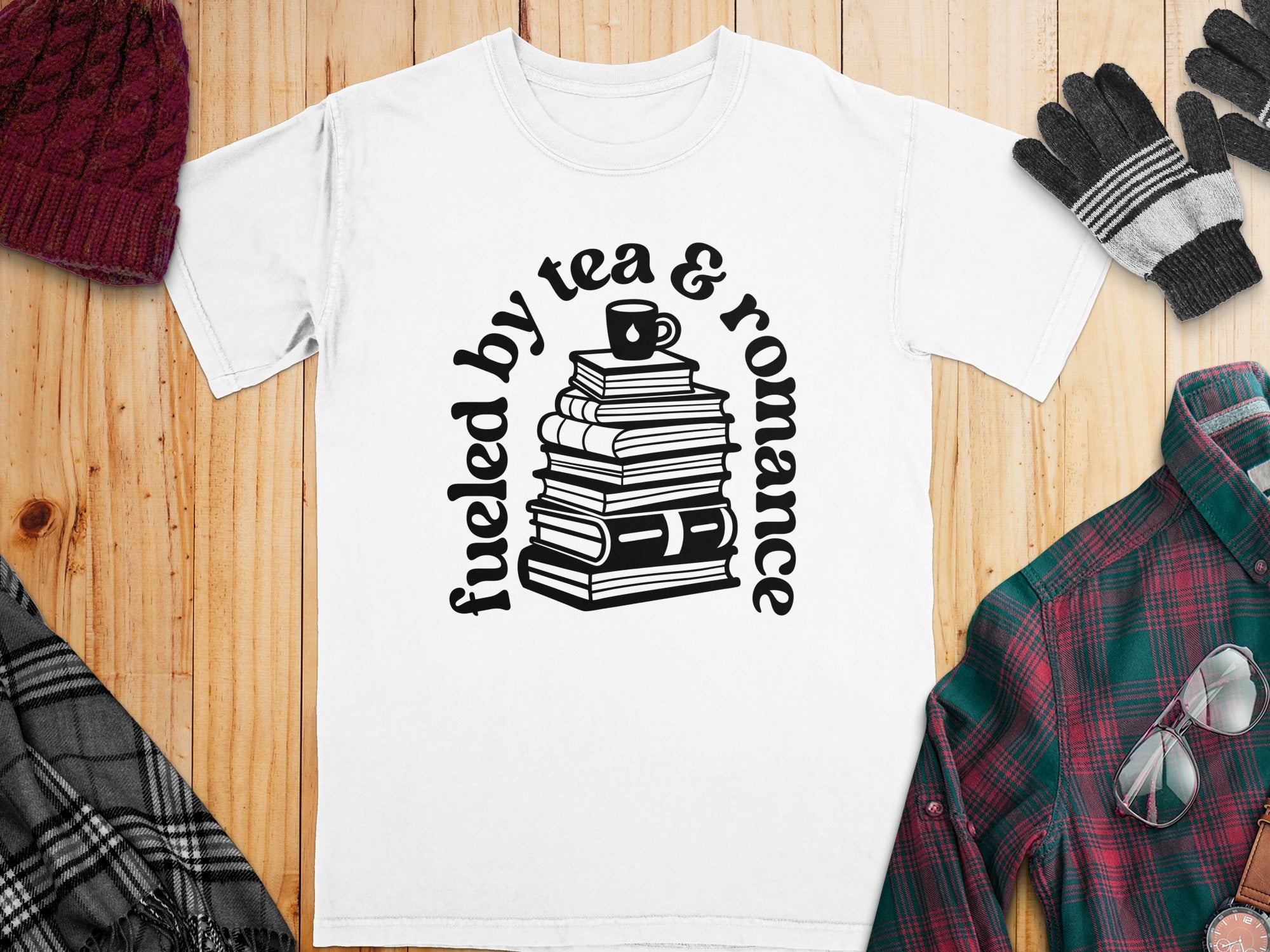 White t-shirt with "fueled by tea & romance" text and a stack of books.