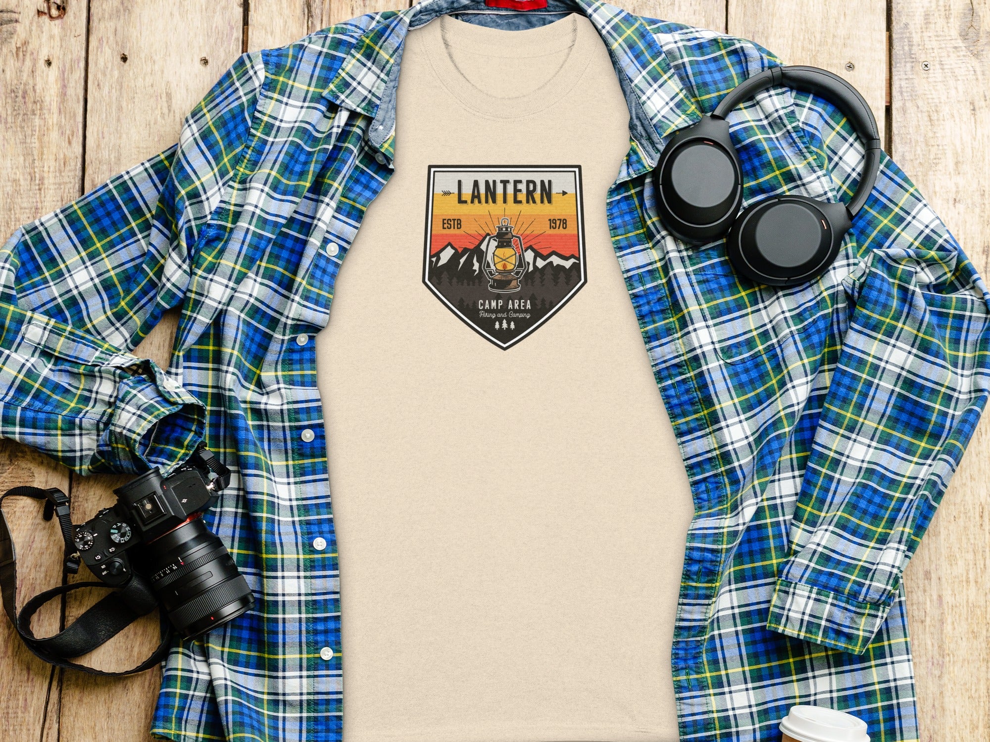 Beige t-shirt with "Lantern Camp Area" graphic, plaid shirt, headphones, and camera.