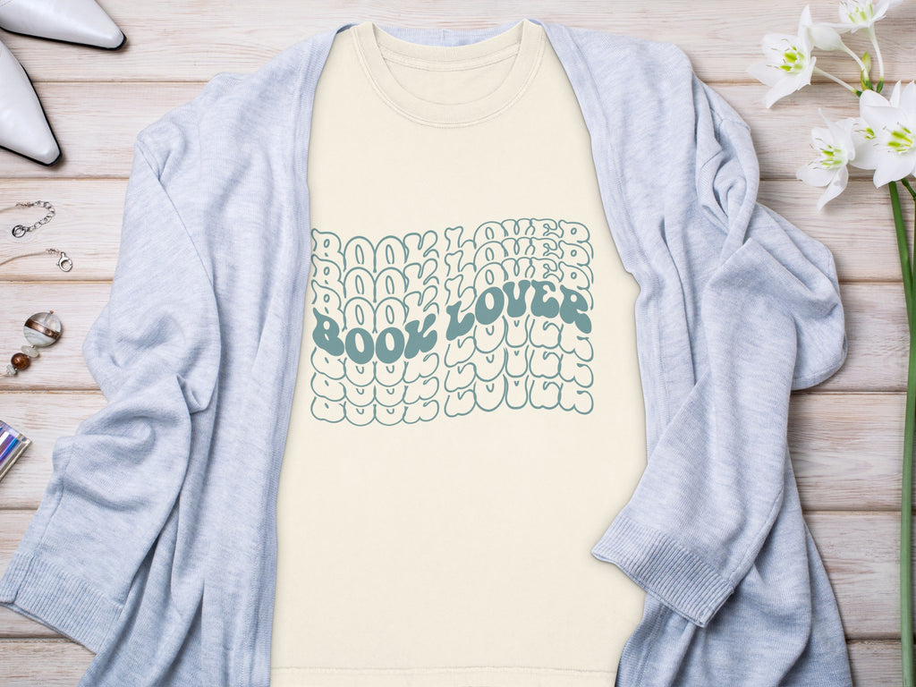 Cream t-shirt with stacked blue "Book Lover" text and bubble-like designs.