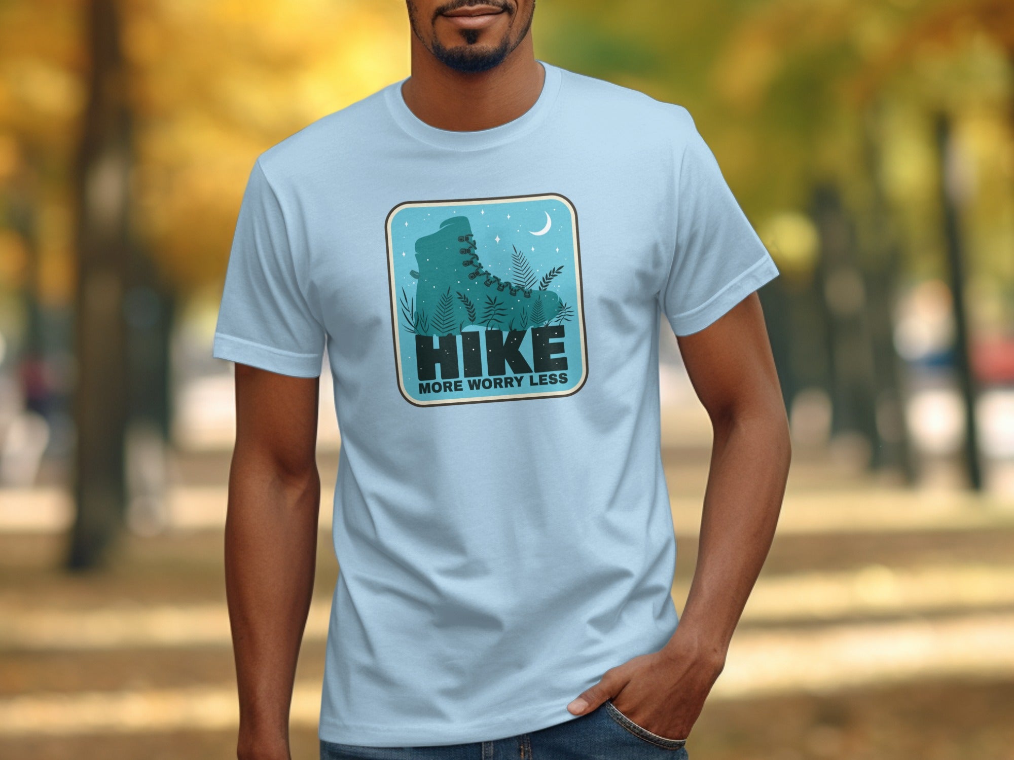 Light blue t-shirt with a graphic of a hiking boot, plants, and text "Hike More Worry Less".