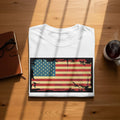 White t-shirt with distressed American flag graphic on a wooden table.