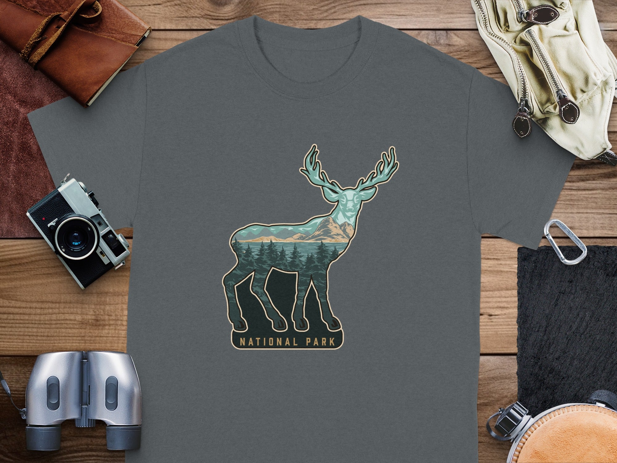 Dark gray t-shirt with deer graphic inside a landscape, showing mountains and trees.