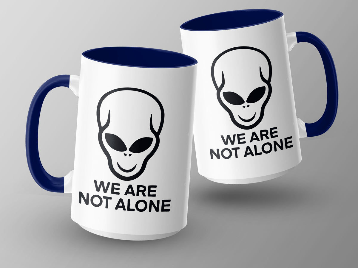 Two white mugs with blue handles and rims, featuring alien faces and "WE ARE NOT ALONE."