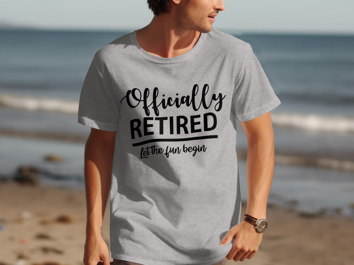 Grey t-shirt with black text "Officially RETIRED let the fun begin" on a beach background.