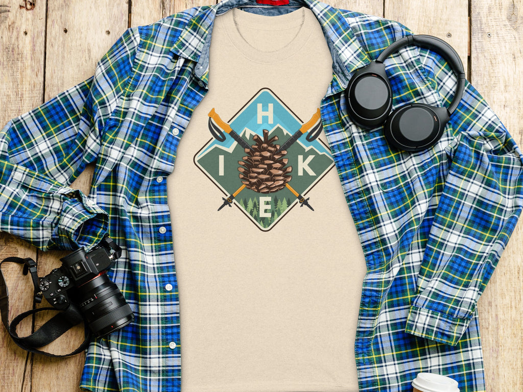 T-shirt with pine cone, hiking poles, mountains, and H, I, K, E letters.