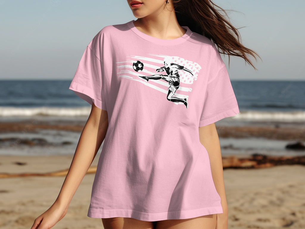 Pink t-shirt with graphic of woman playing soccer with American flag design.