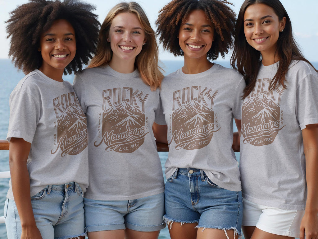 Four smiling women wear grey t-shirts with a "Rocky Mountains National Park Est. 1975" mountain graphic.