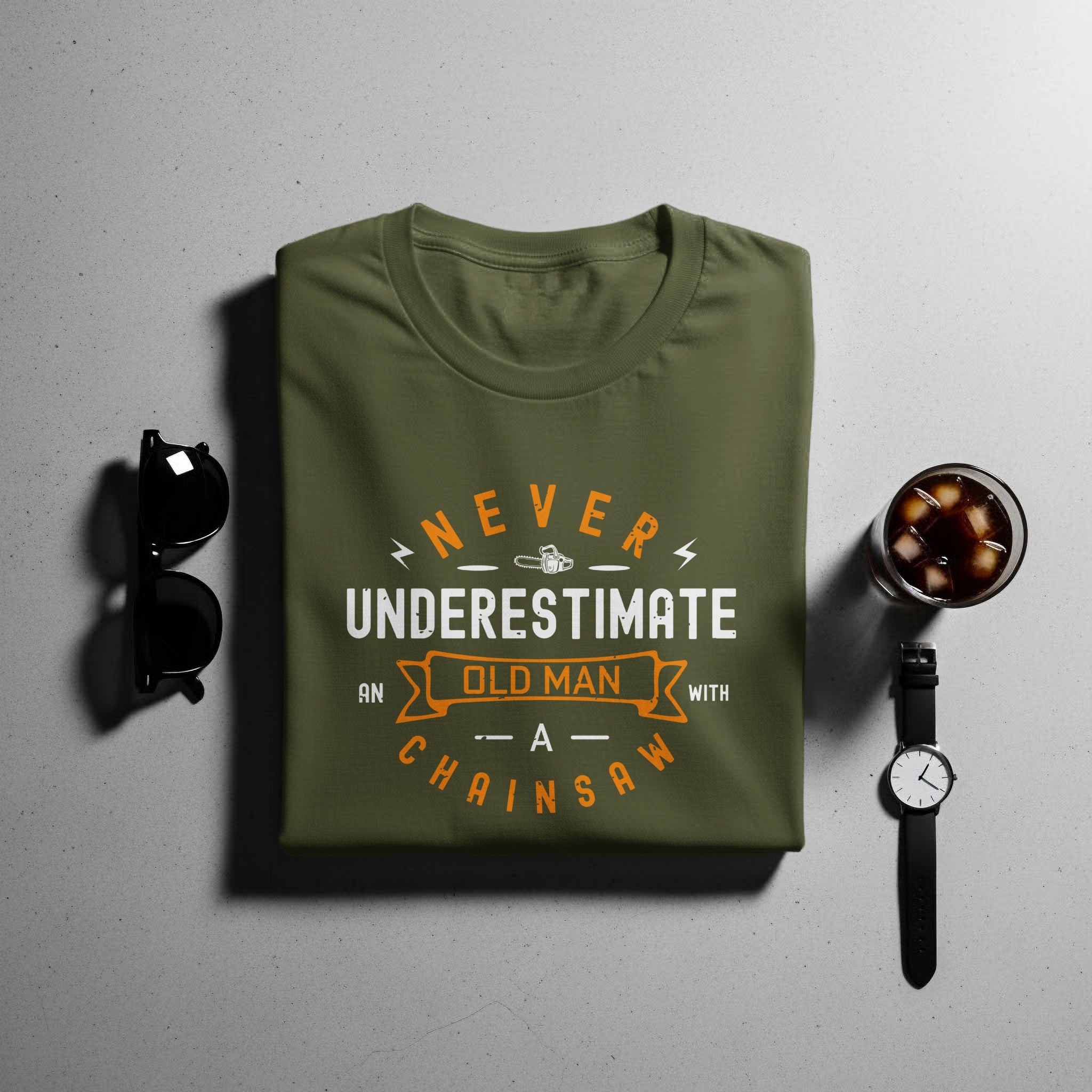 Olive green t-shirt with "Never Underestimate An Old Man With A Chainsaw" graphic.