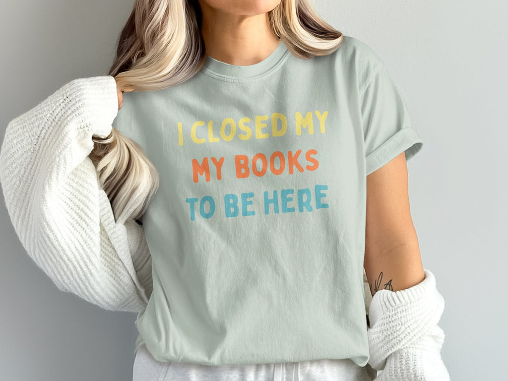 Light mint t-shirt with yellow, orange, and blue text: "I CLOSED MY MY BOOKS TO BE HERE".