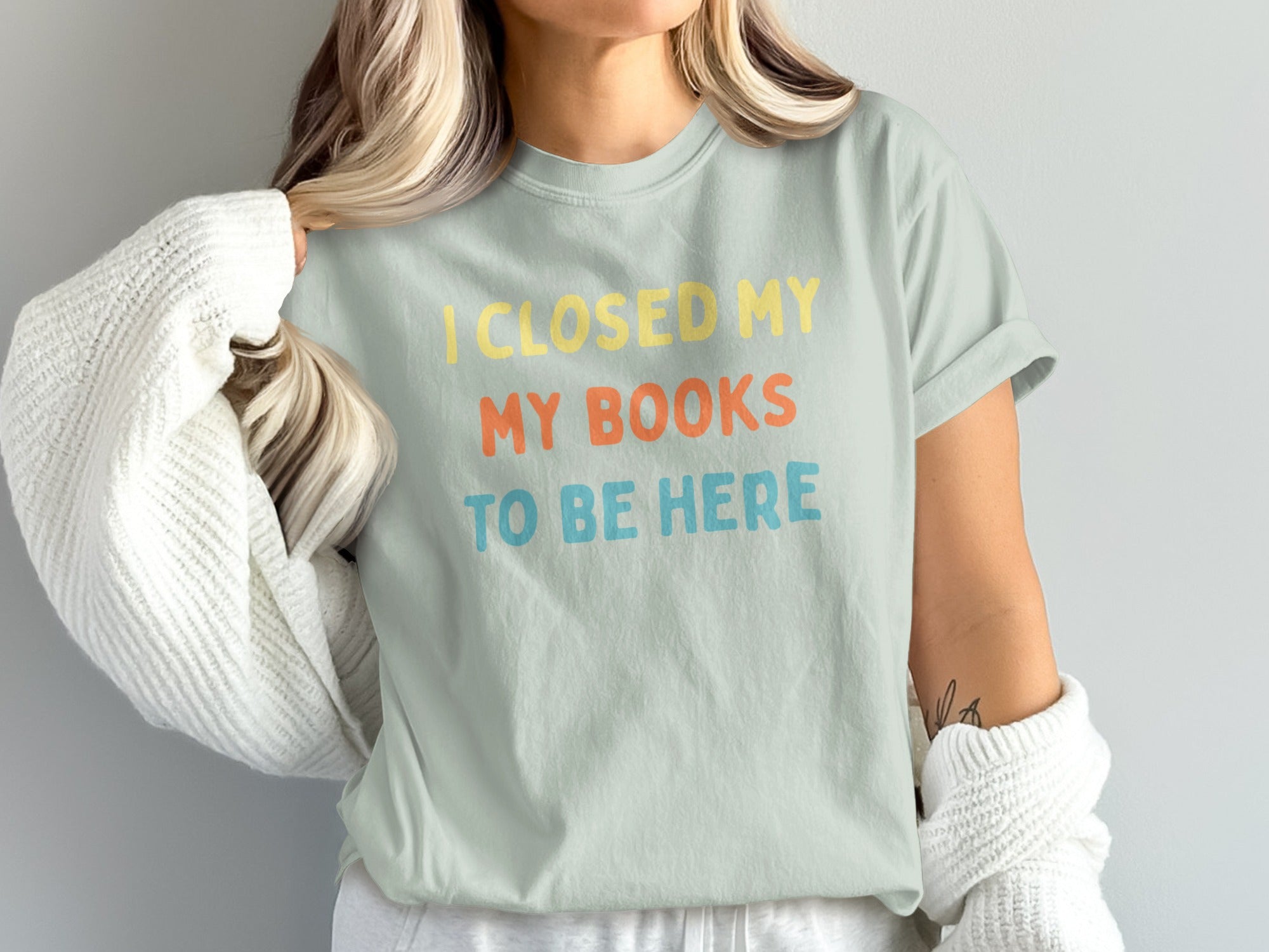 Light mint t-shirt with yellow, orange, and blue text: "I CLOSED MY MY BOOKS TO BE HERE".